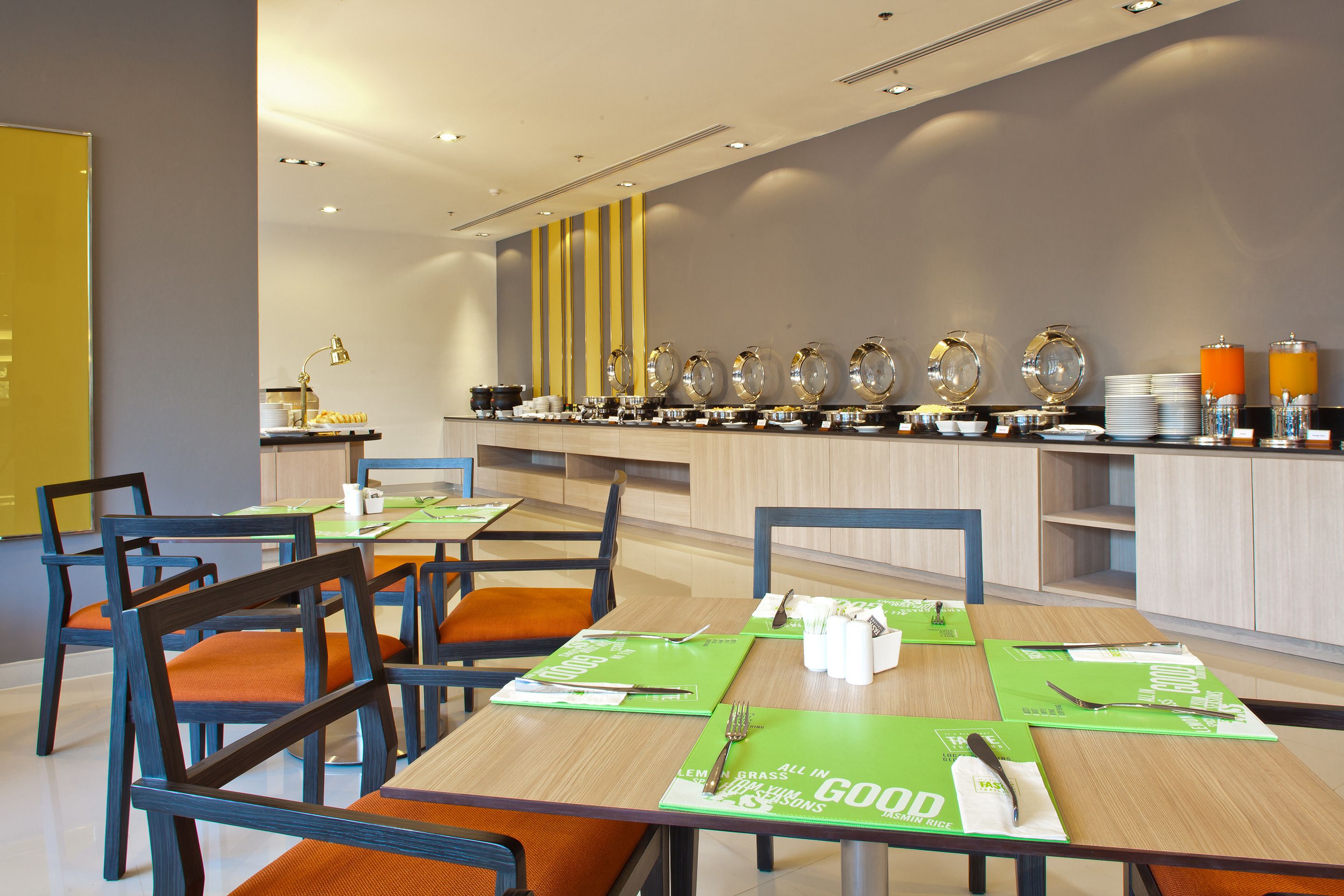 A modern dining area with wooden tables, green placemats, and orange chairs.