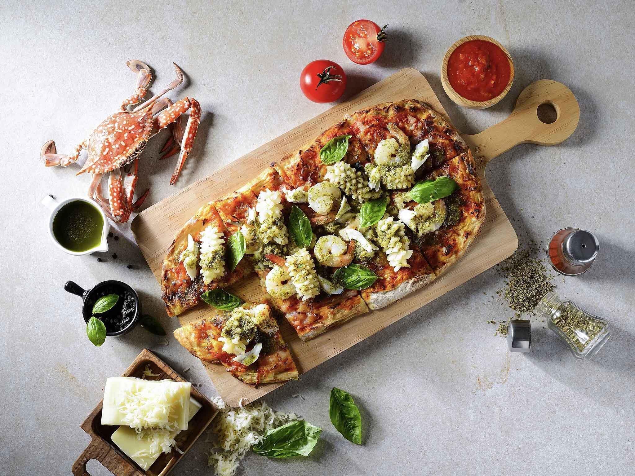 Una pizza sobre una tabla de madera con diferentes ingredientes, rodeada de otros ingredientes y utensilios.
