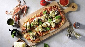 Una pizza sobre una tabla de madera con diferentes ingredientes, rodeada de otros ingredientes y utensilios.