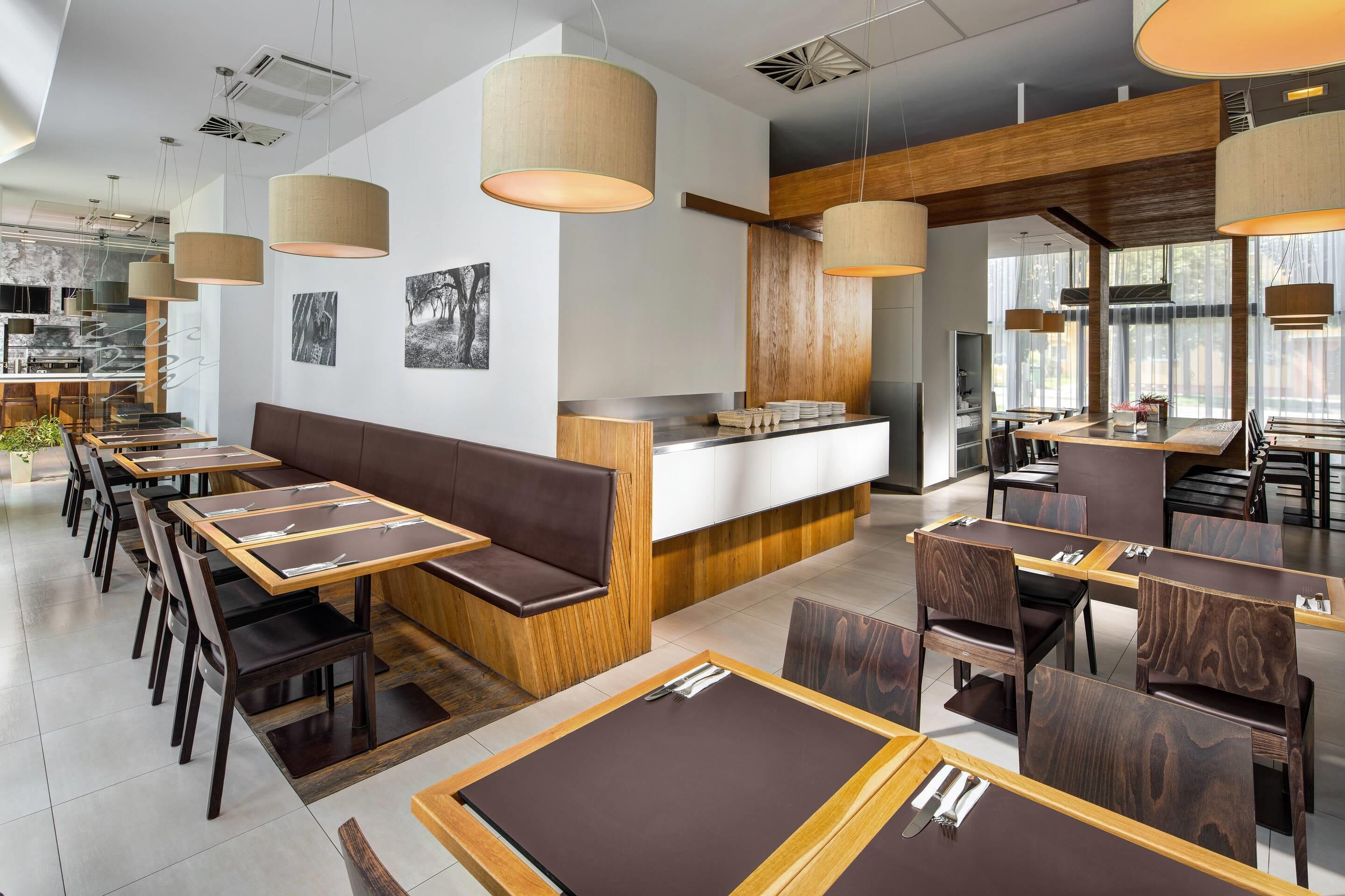 A modern restaurant interior with wooden tables, cushioned booths, and pendant lighting.