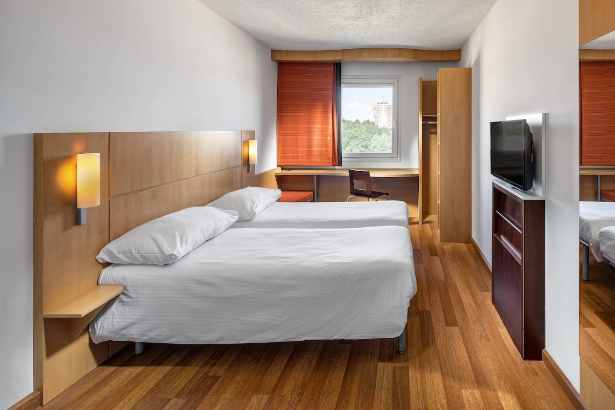 Una habitación de hotel con dos camas, un escritorio, un televisor y una ventana con persianas.