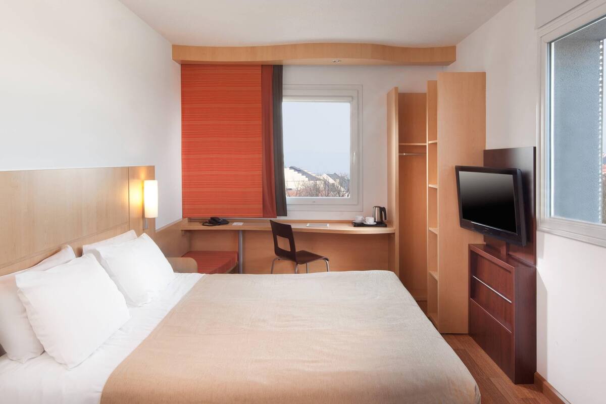 Una habitación de hotel con cama, escritorio, silla, televisión y ventana con vistas.