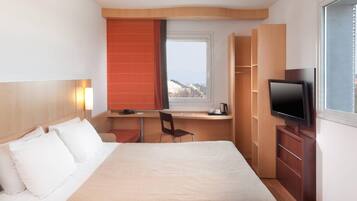 Een hotelkamer met een bed, een bureau, een stoel, een televisie en een raam met uitzicht.