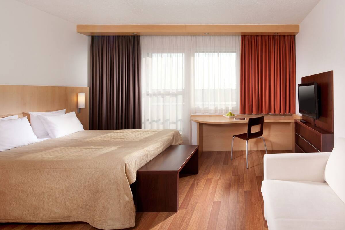 Habitación de hotel con cama, escritorio, silla, televisión y sofá.
