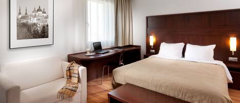 A hotel room with a large bed, a desk with a laptop, a chair, a bench, a couch, and a framed picture on the wall.