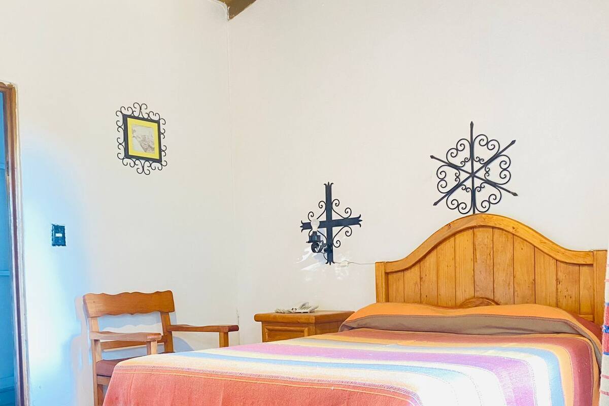 Ein Schlafzimmer mit einem hölzernen Bett, einem Nachttisch, einem Stuhl und einem an der Wand befestigten Kreuz.