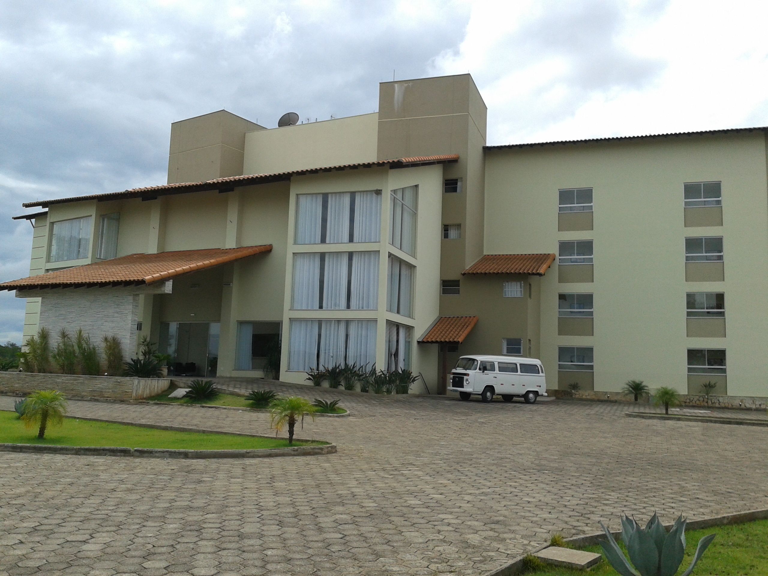 Un edificio de varios pisos con techo plano, ventanas grandes y una furgoneta blanca estacionada al frente.