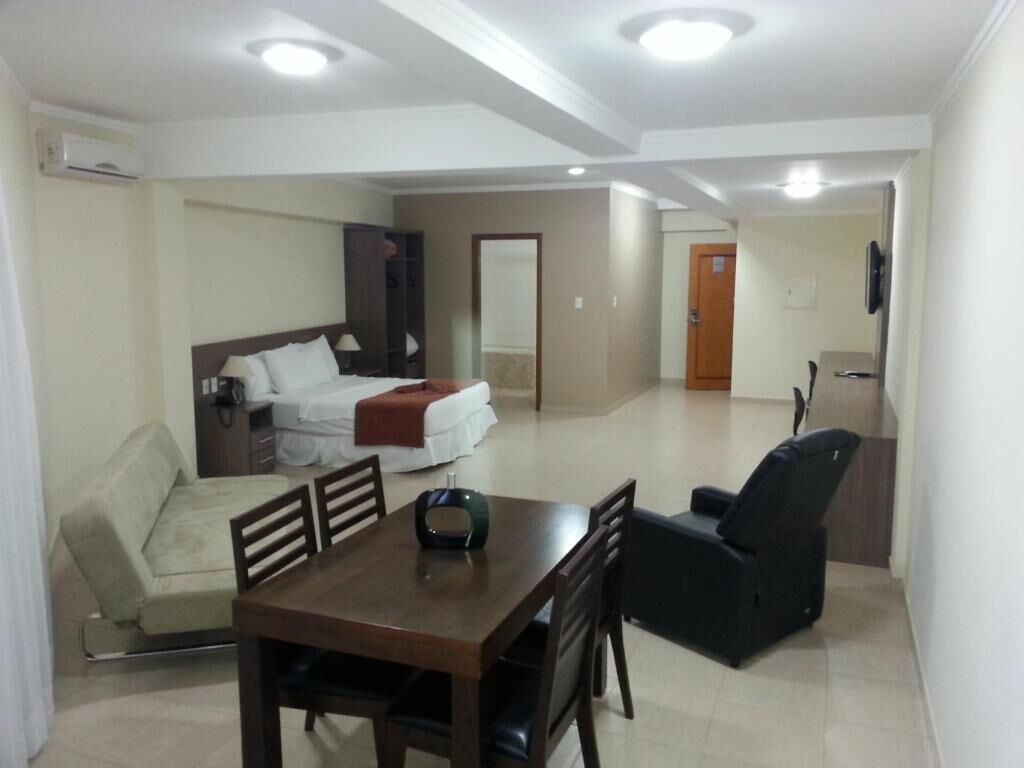 A hotel room with a bed, a sofa, a dining table with chairs, and a TV.