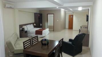A hotel room with a bed, a sofa, a dining table with chairs, and a TV.