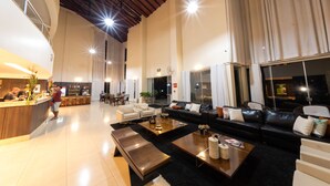 A spacious hotel lobby with a high ceiling, a reception area, seating arrangements, and large windows. - Class Hotel Passos Rio Grande Portal da Canastra (Passos)