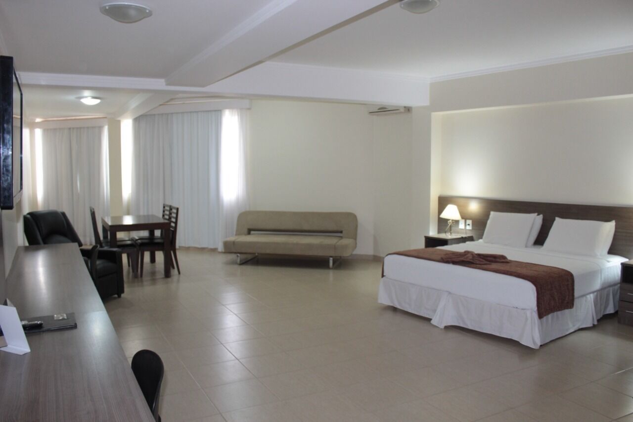 Una habitación de hotel con cama, sofá, mesa de comedor y sillas, y televisión.