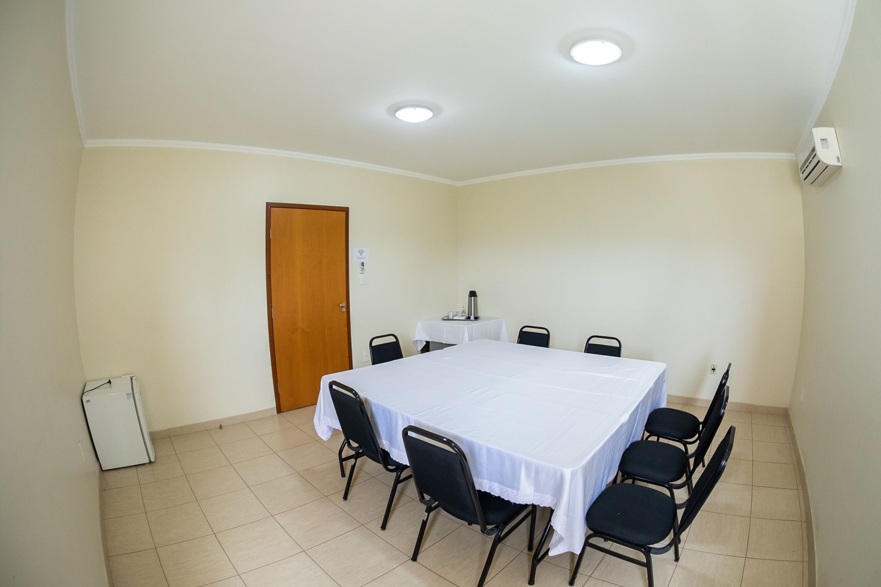 A conference room with a large table, chairs, a door, and a small refrigerator.