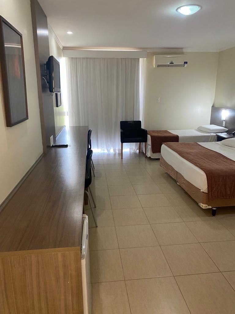 Une chambre d’hôtel avec un bureau en bois, deux lits, une chaise et un téléviseur.