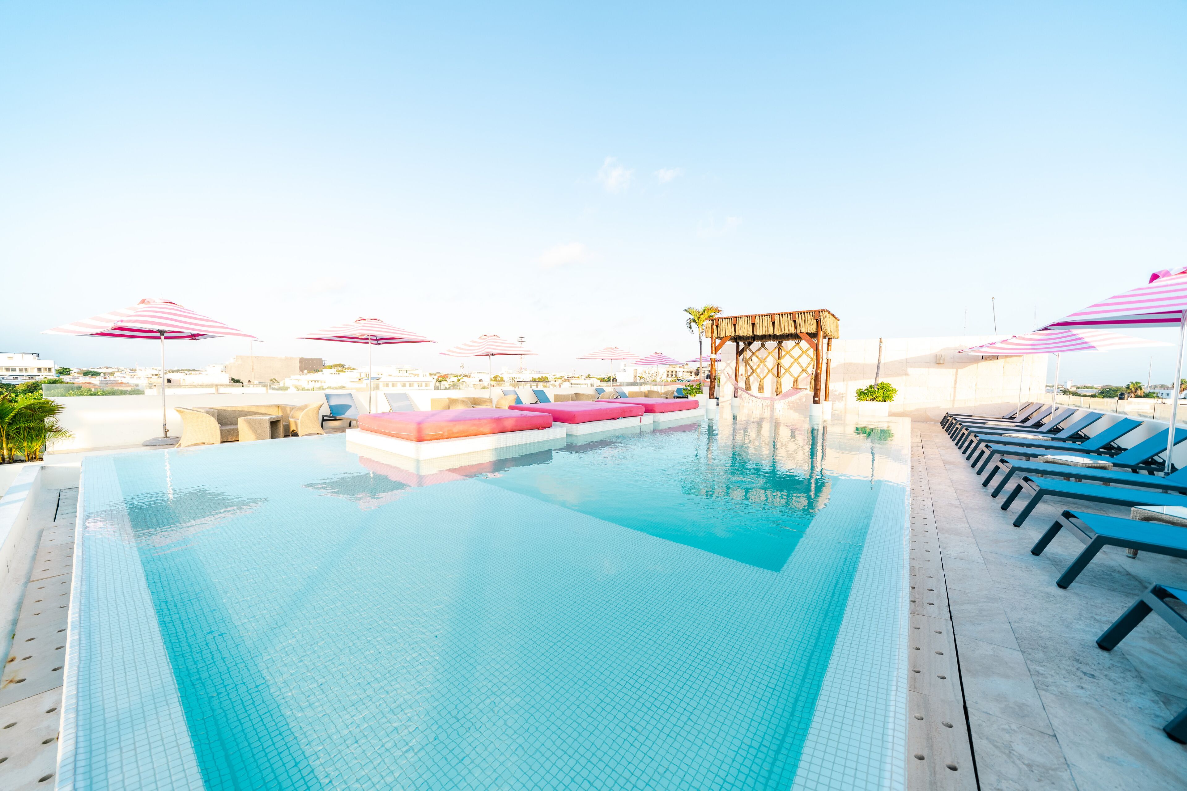 A rooftop pool with clear blue water, sun loungers, and pink-striped umbrellas.