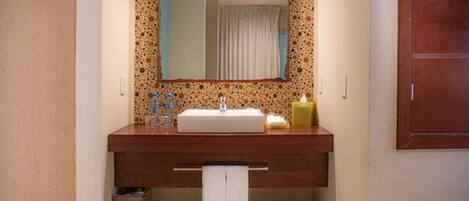 Un baño con tocador de madera, espejo, lavabo y perchero para toallas.