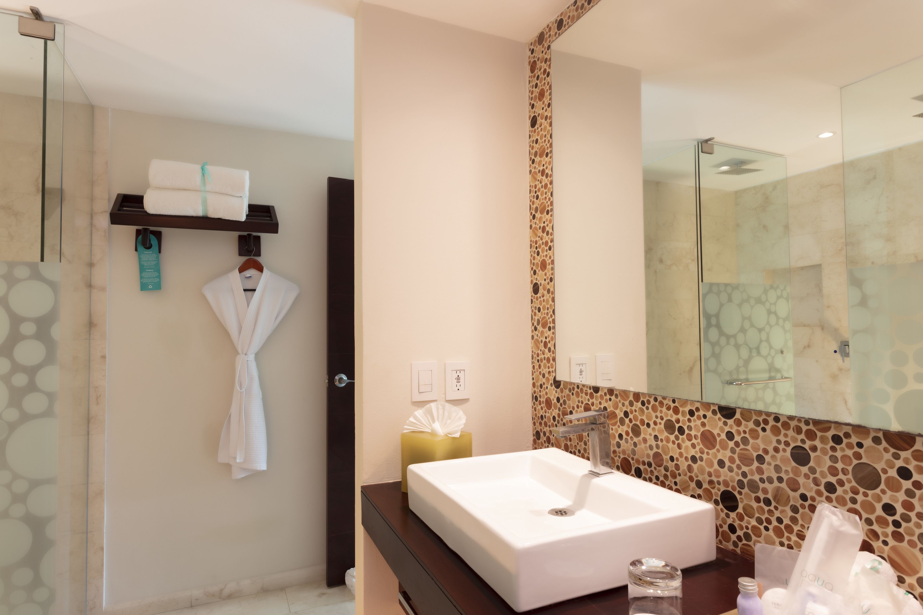 Un baño moderno con un espejo grande, un lavamanos blanco y un perchero para toallas.