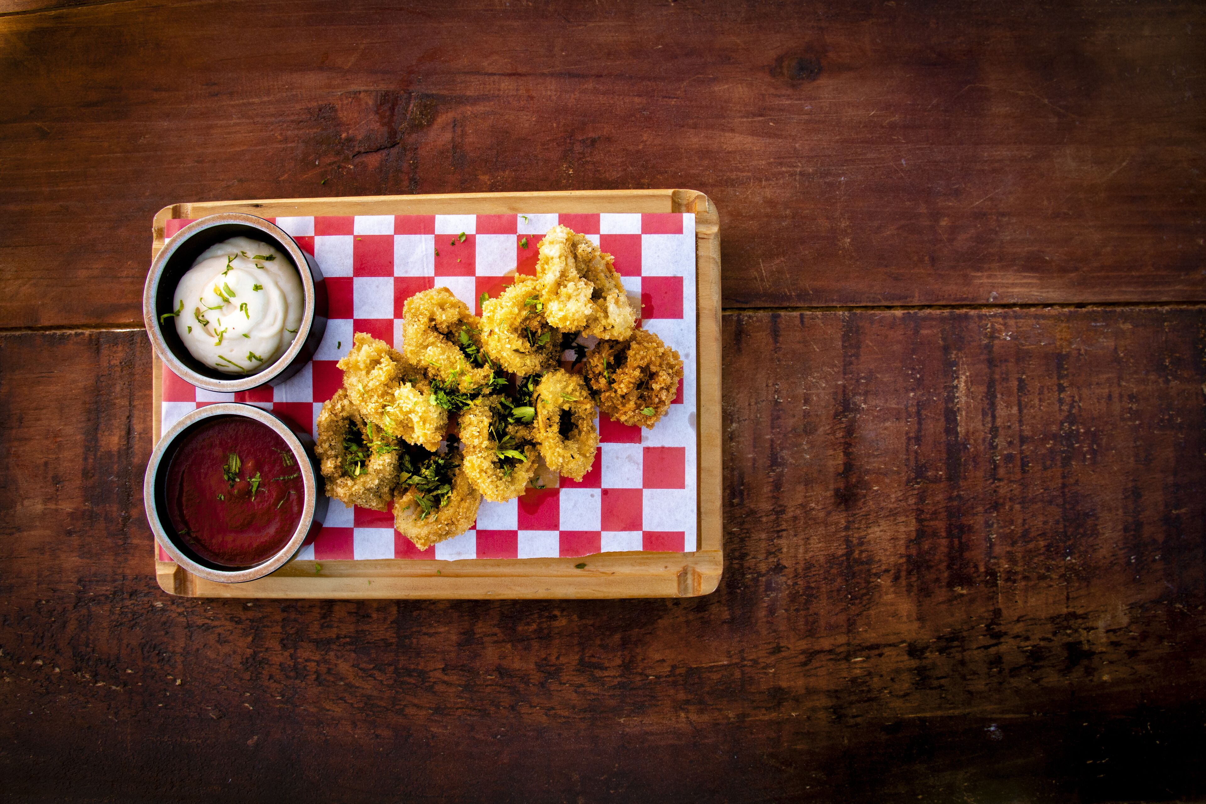 A wooden table with a checkered paper under a tray of fried food and two dipping sauces.