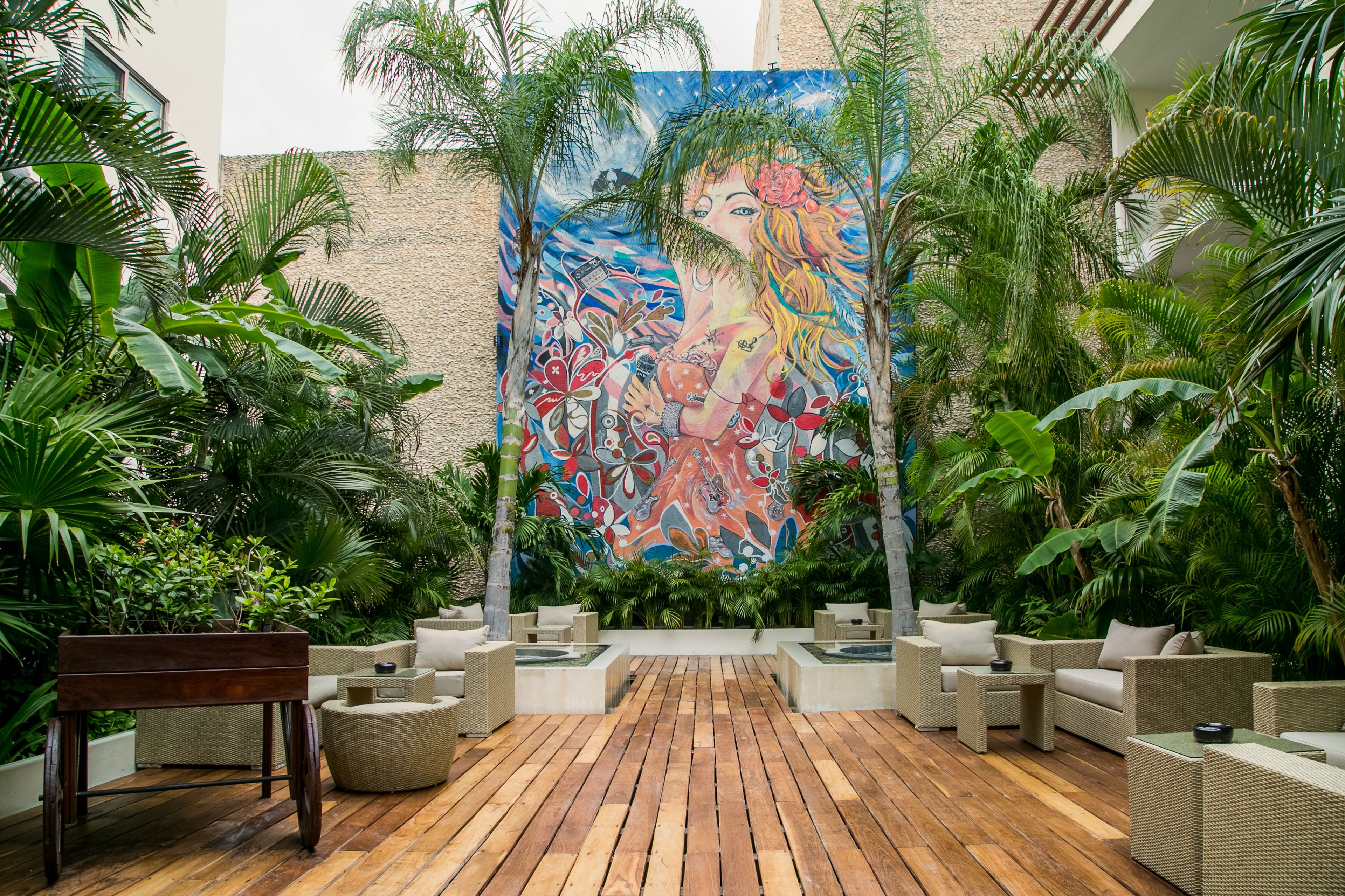 A tropical garden with a mural, wooden flooring, and wicker furniture.