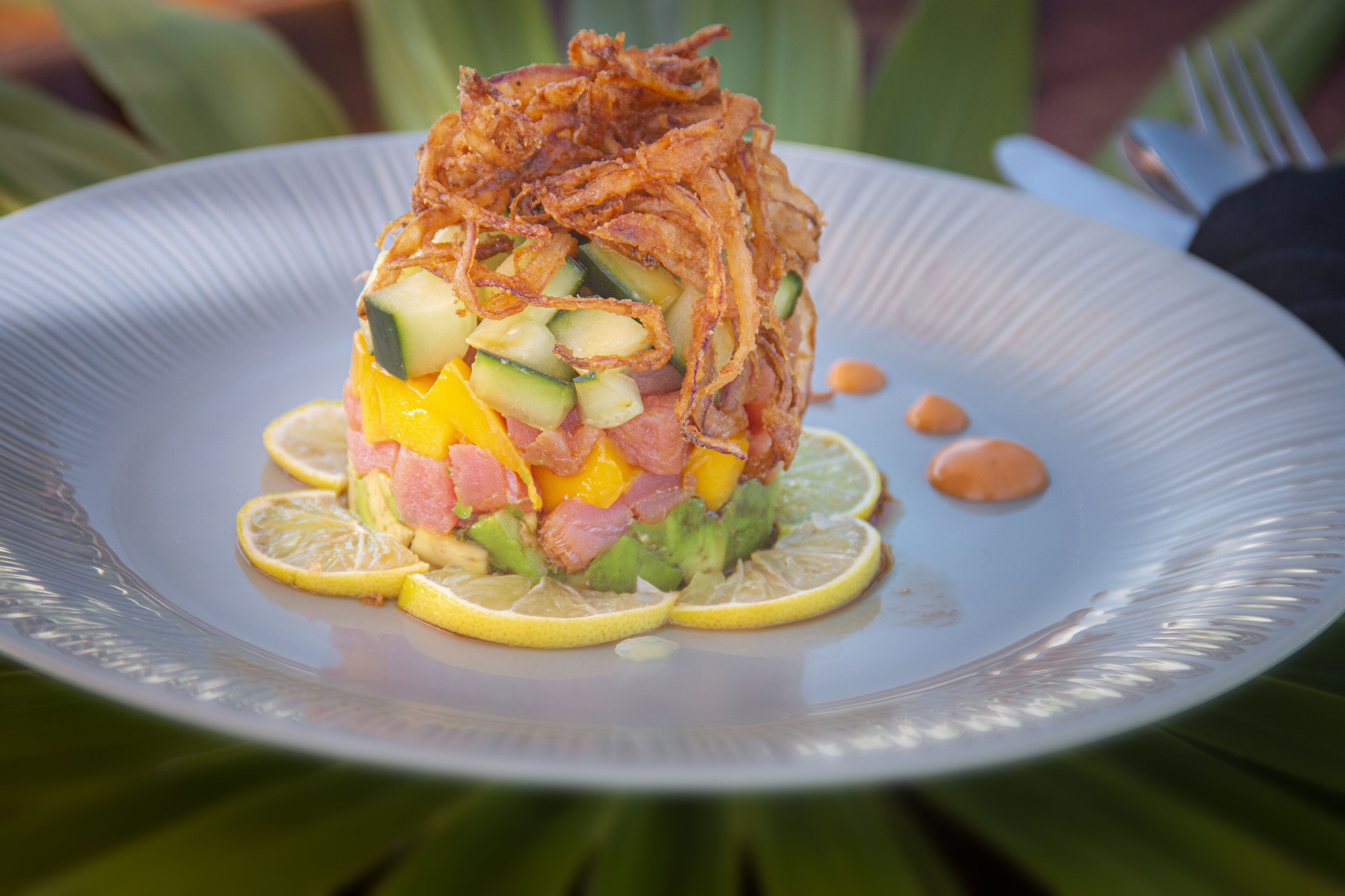 Un plato con ensalada en capas, coronado con cebollas fritas y rodajas de limón.