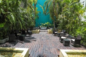 Un patio con mobiliario de mimbre, una fuente bordeada de guijarros y exuberante vegetación tropical.