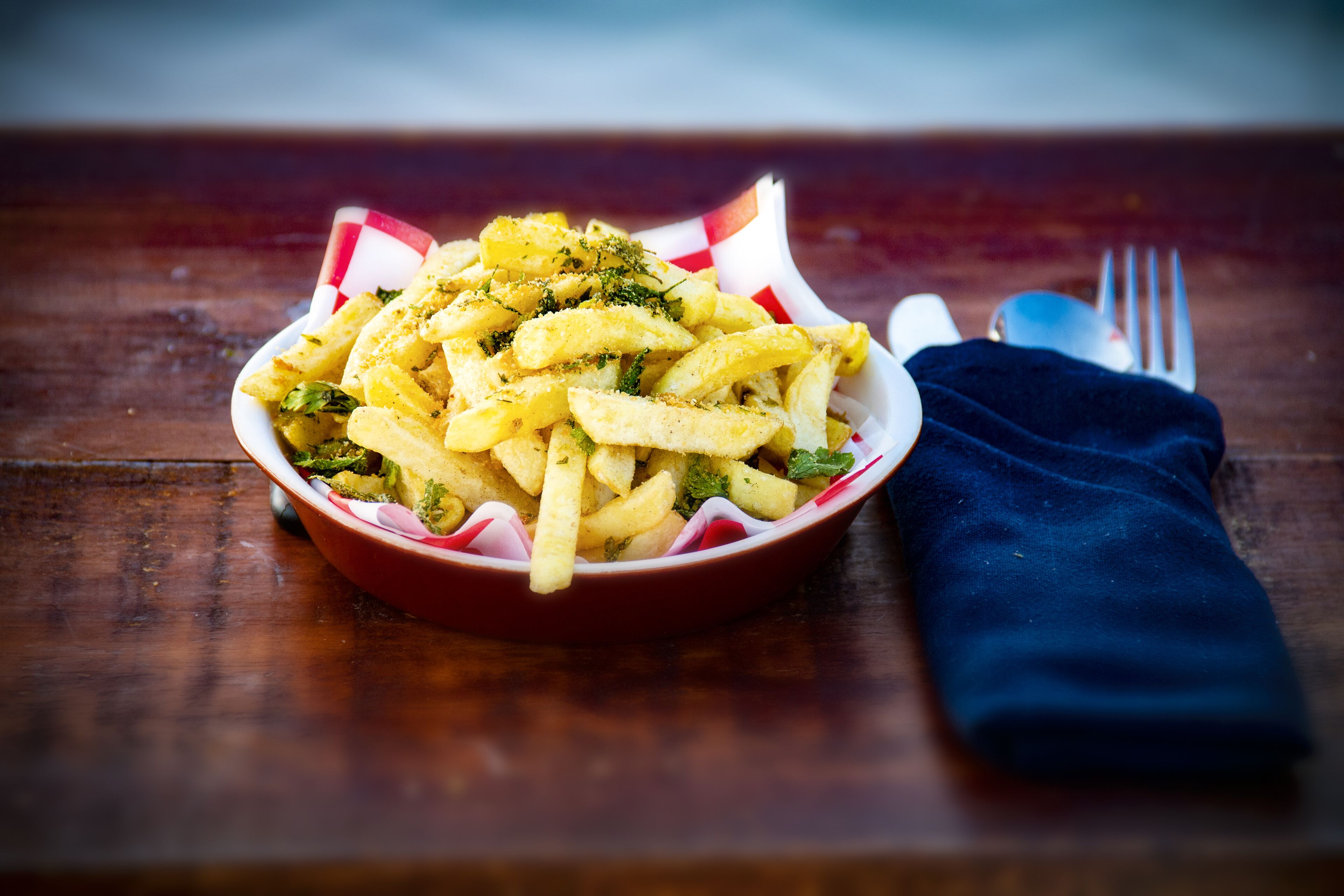 Un bol de frites, une serviette bleue et une fourchette sur une table en bois.