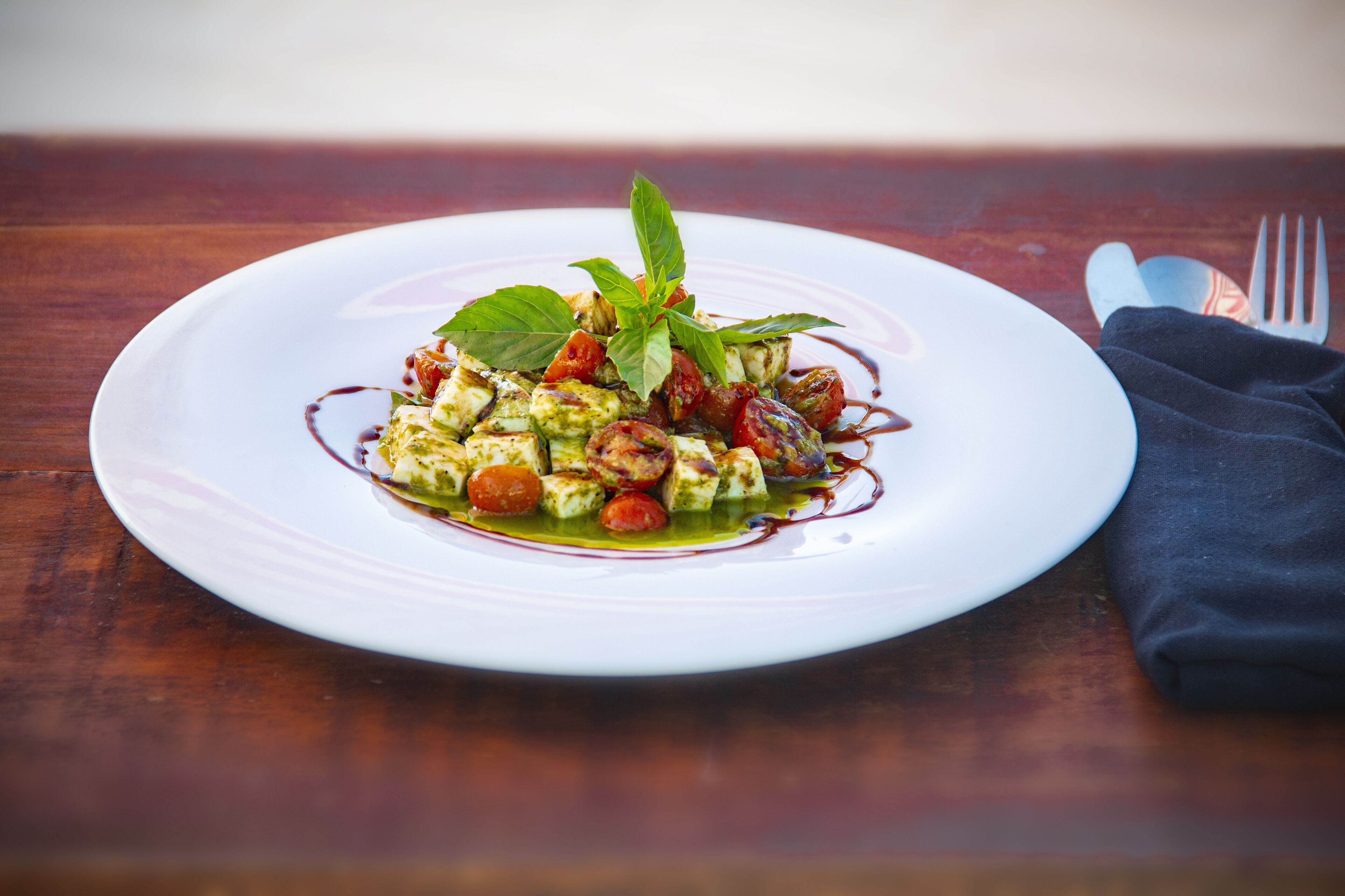 A white plate with a dish of food, a fork, and a napkin on a wooden table.