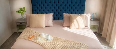 Een net opgemaakt bed met een blauw hoofdbord, twee nachtkastjes met lampen en een geweven plaids.