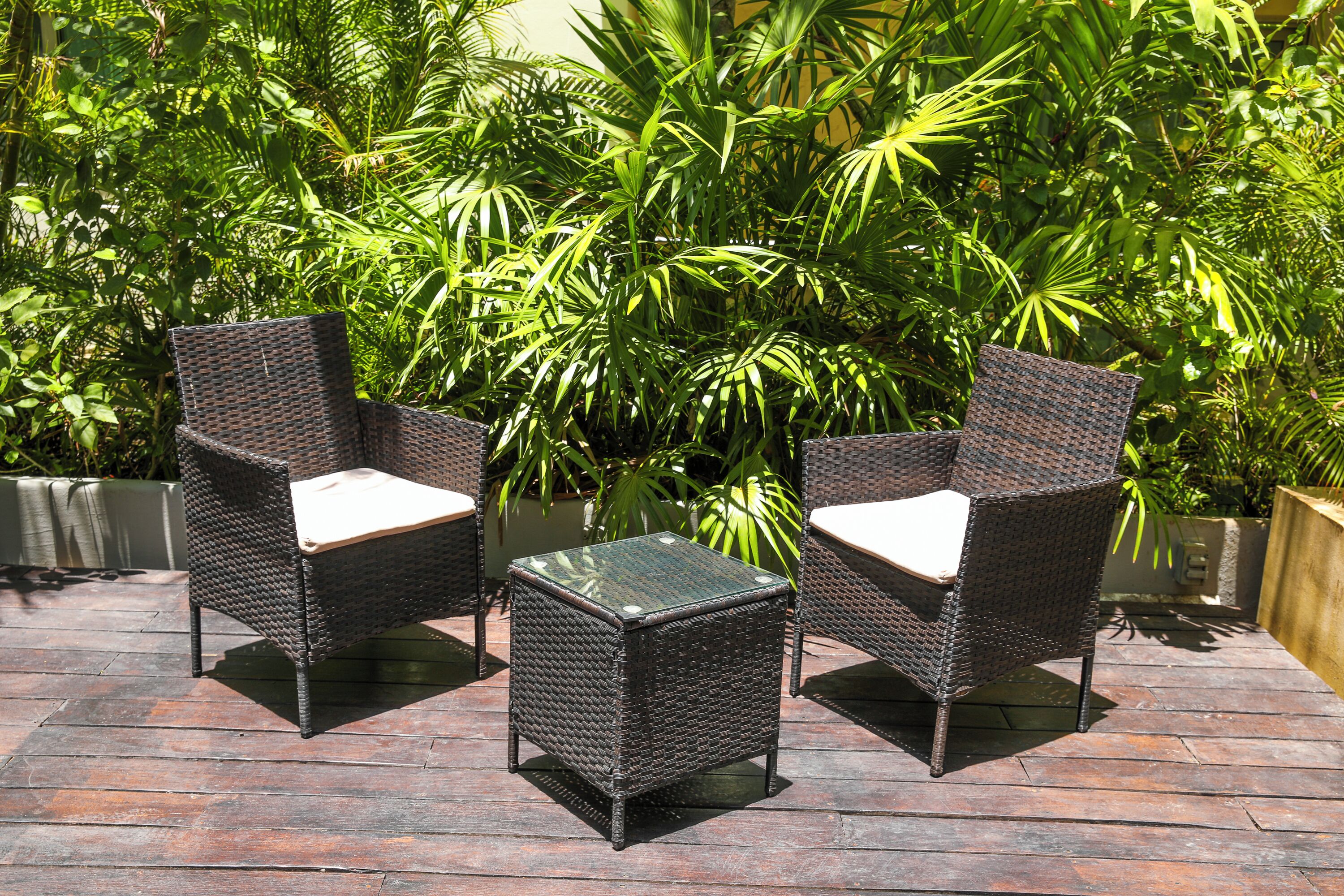 Deux fauteuils en osier avec des coussins et une petite table carrée sur une terrasse en bois.