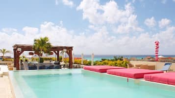 A pool area with lounge chairs and a wooden pergola, overlooking a beach and ocean.