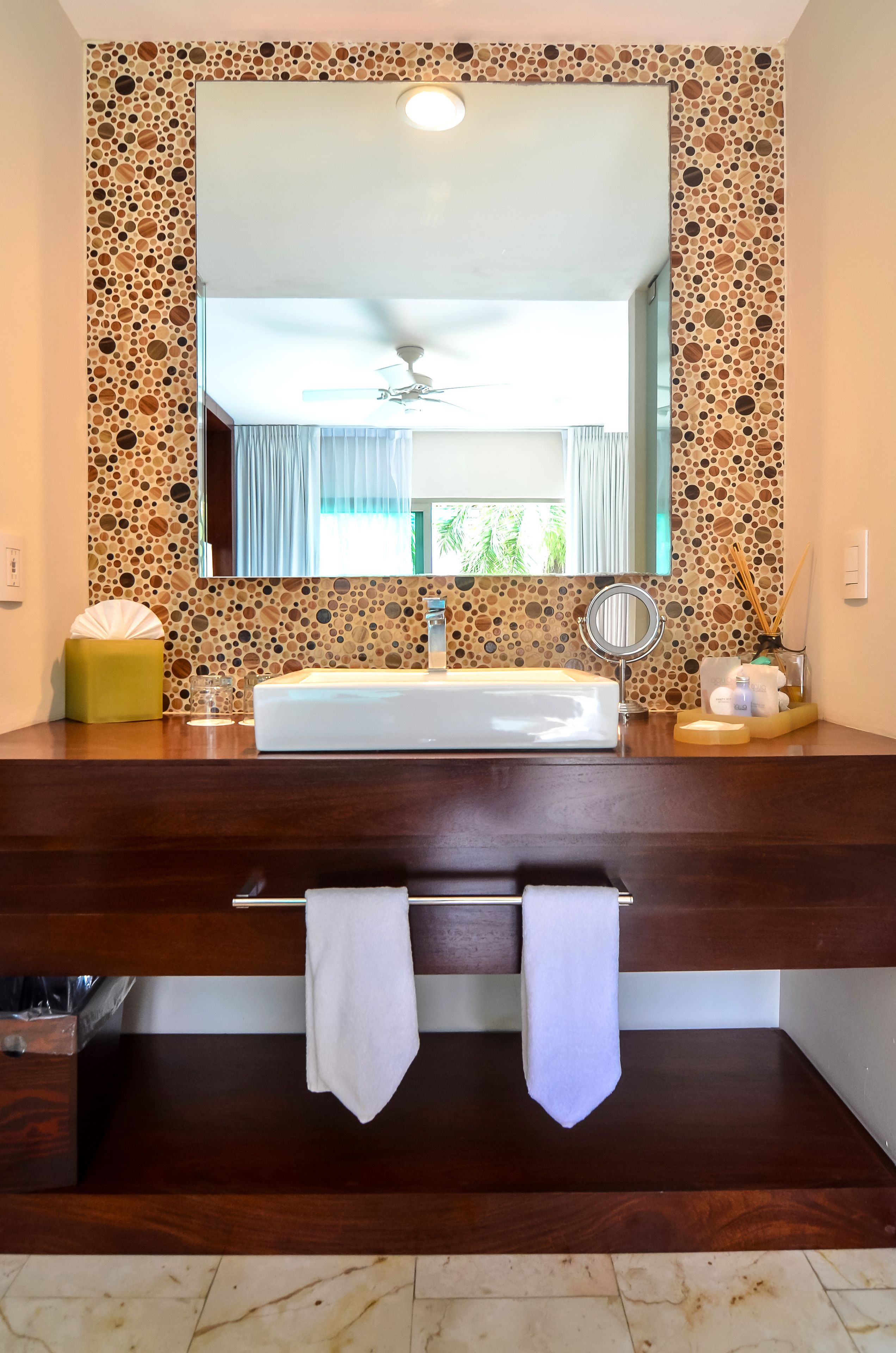 Une salle de bain avec un grand miroir, un lavabo blanc et un meuble-lavabo en bois.