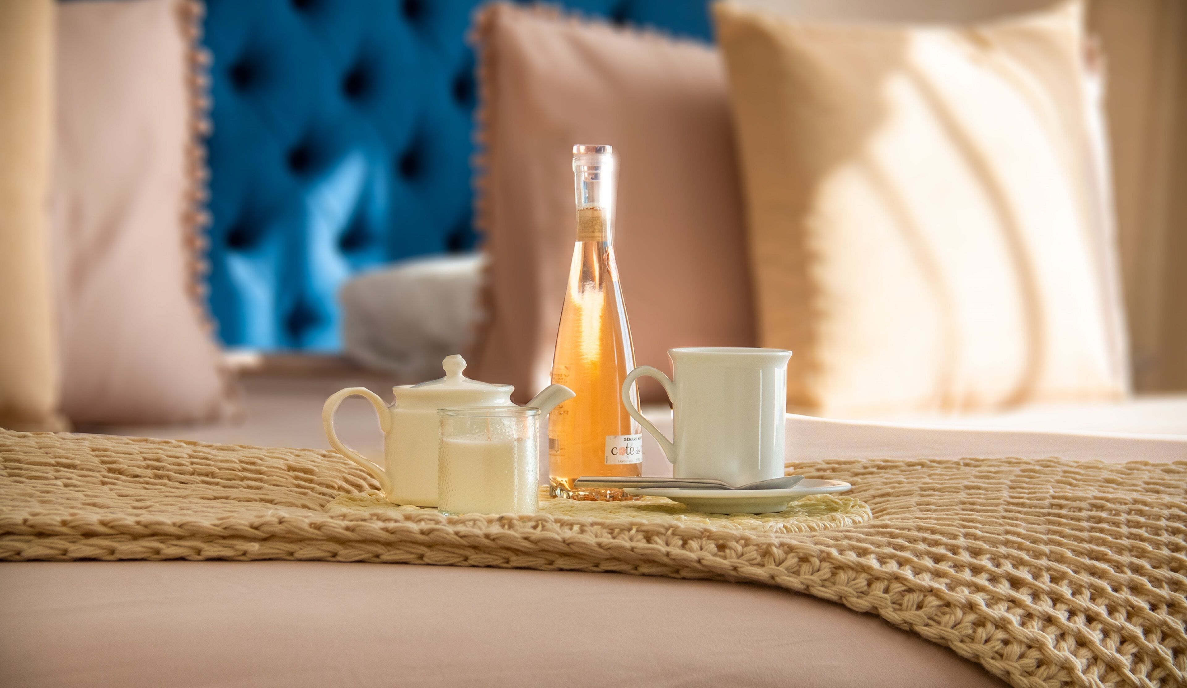 A breakfast setup with a teapot, cup, saucer, and a bottle on a woven placemat.