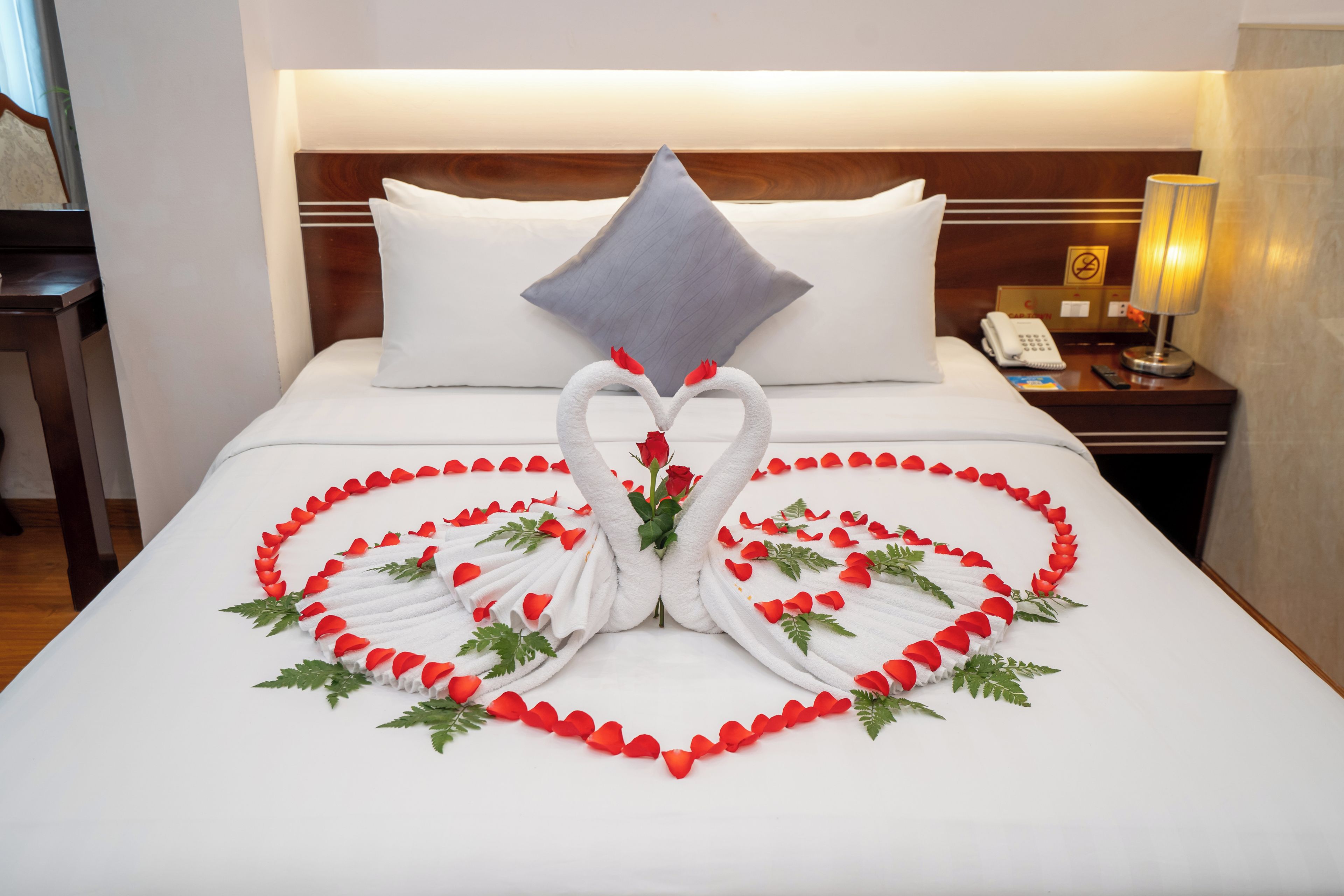 Habitación de hotel con cama bien hecha, cabecera, mesita de noche con lámpara y teléfono.