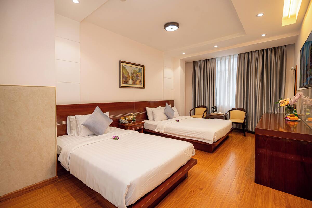 A hotel room with two beds, a desk, a chair, and a painting on the wall.