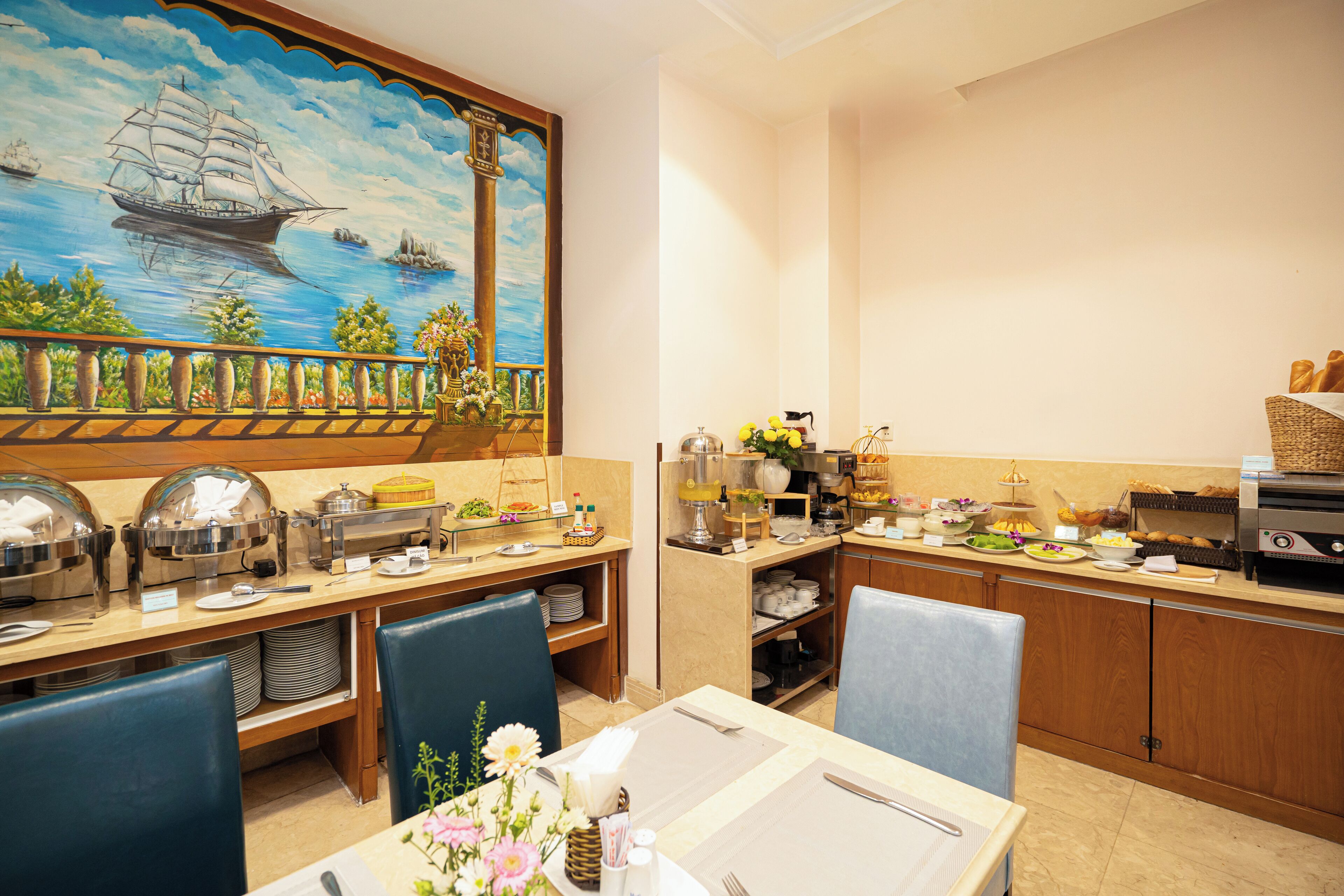 A buffet setup with various food items and a mural of a sailing ship on the wall.