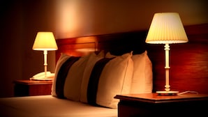A hotel room with a bed, two bedside lamps, and a wooden headboard.