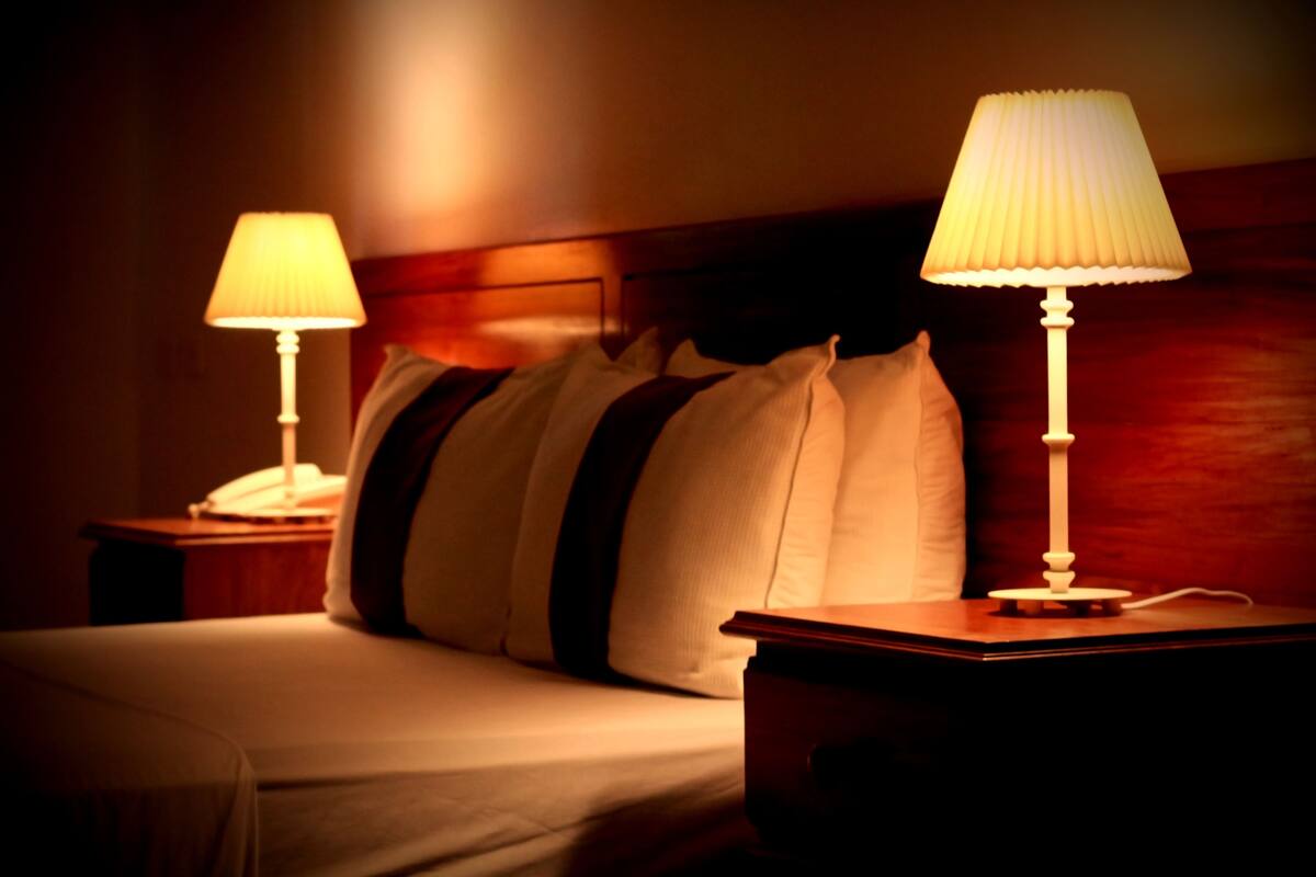 Een hotelkamer met een bed, twee bedlampjes en een houten hoofdeinde.
