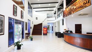 A modern hotel lobby with a reception desk, a staircase, and framed artwork on the walls.