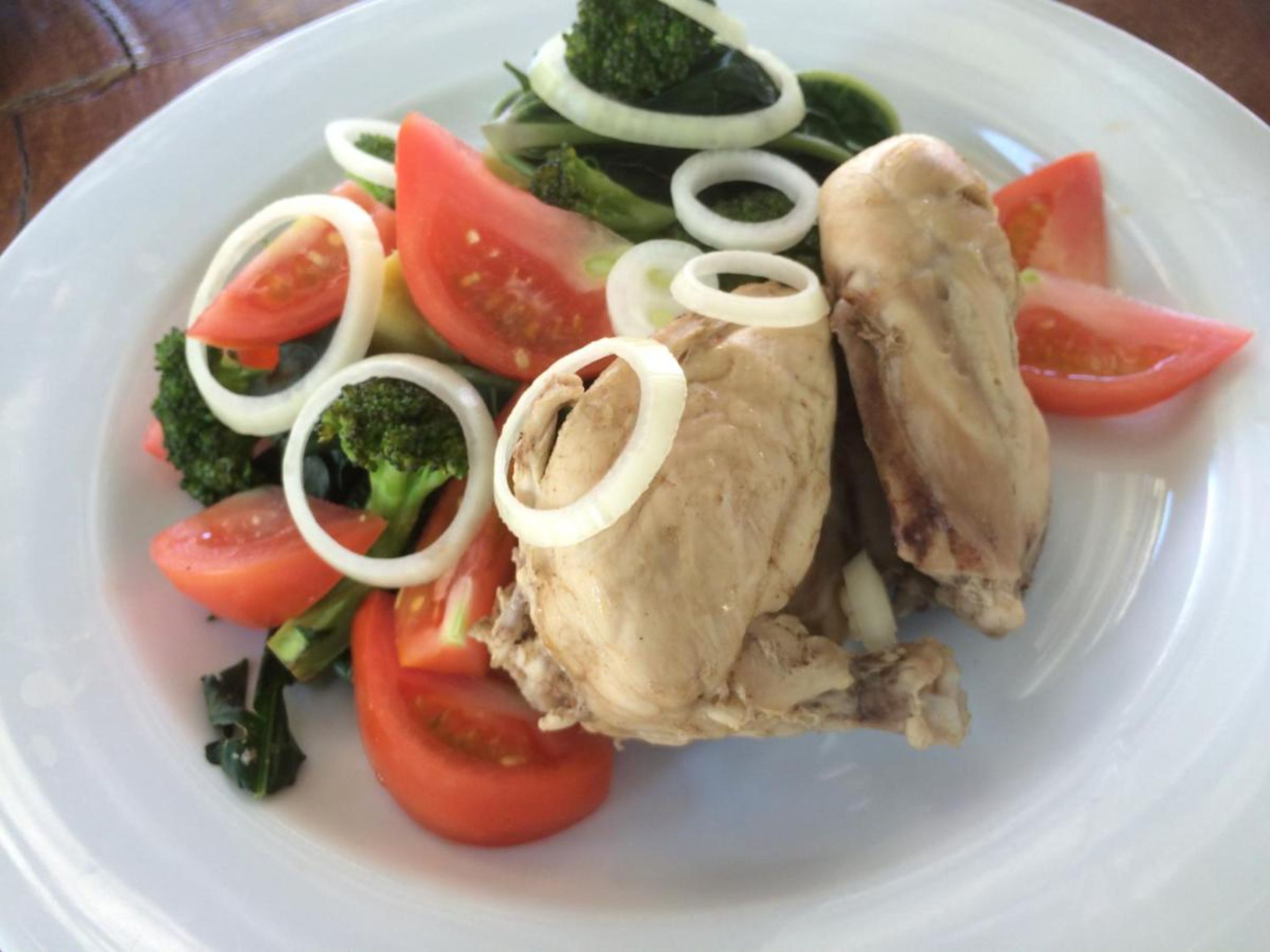 Un plato con pollo en rodajas, tomates, brócoli y cebollas.