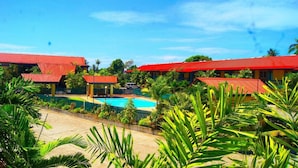 A resort with multiple red-roofed buildings, a central swimming pool, and lush tropical vegetation.