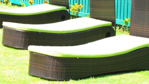 Three outdoor lounge chairs with green cushions, arranged in a row on a grassy lawn, with a blue picket fence in the background.