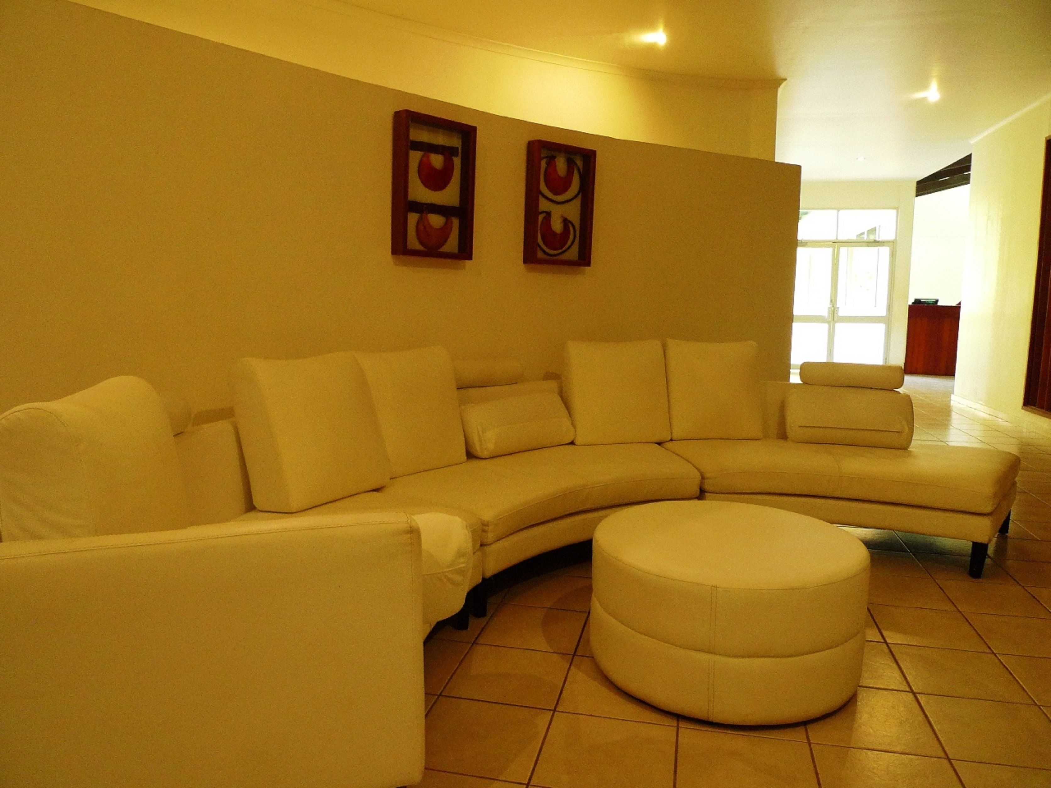 A living room with a beige sectional sofa, a round ottoman, and two framed artworks on the wall.