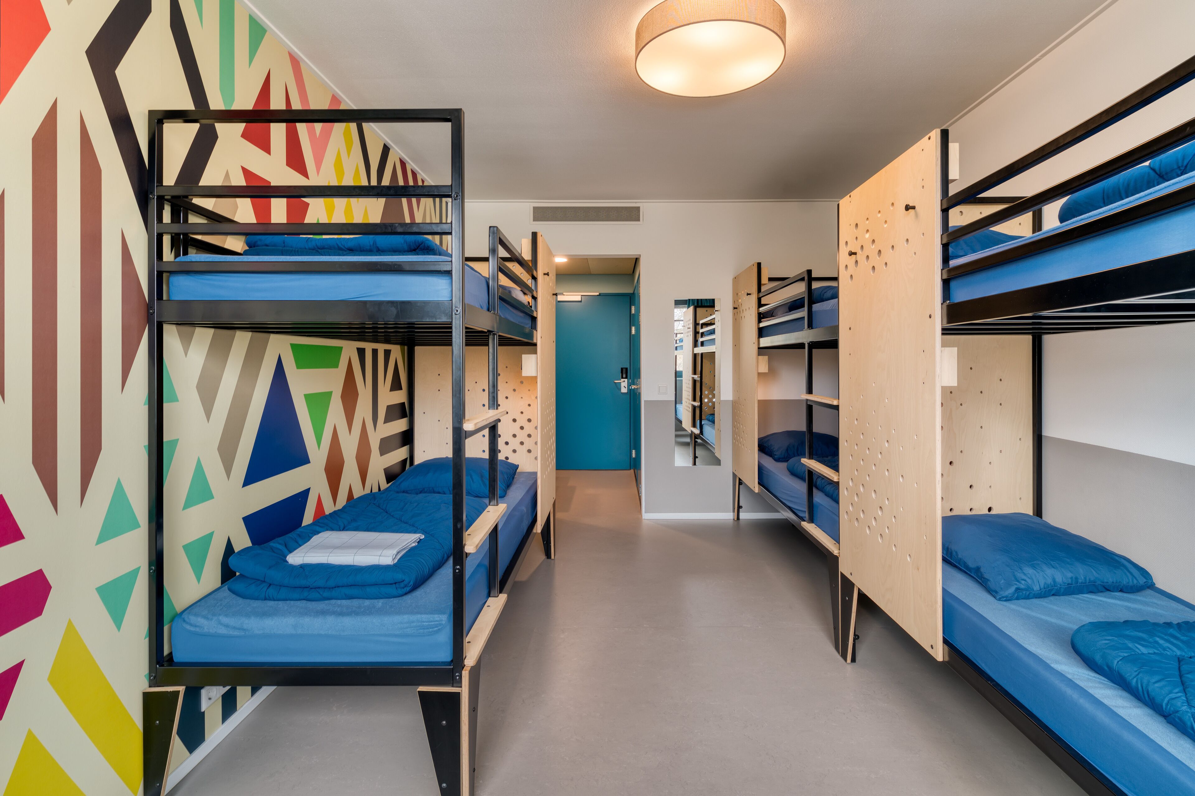 Un dormitorio con literas, una pared con motivos geométricos y un colorido diseño, y una puerta que da a otra habitación.