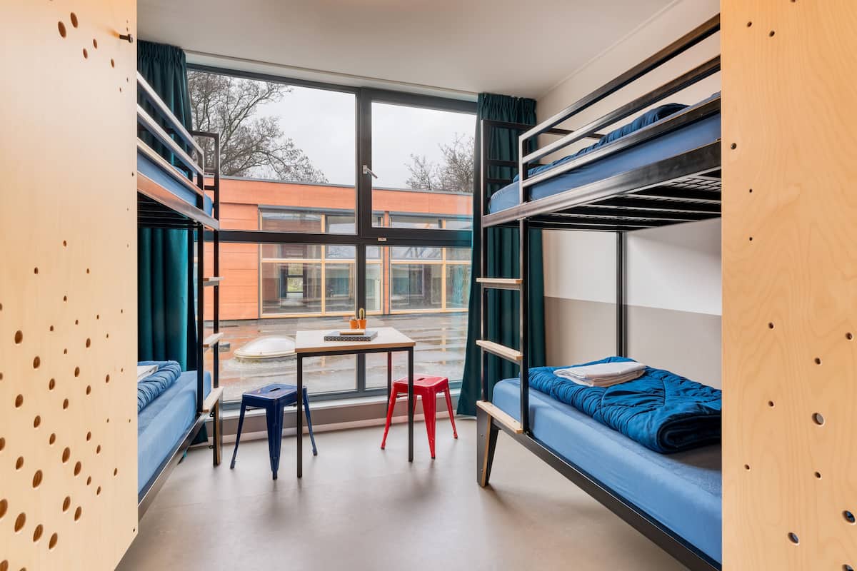 Une chambre de dortoir avec des lits superposés, une petite table et une fenêtre avec des rideaux.