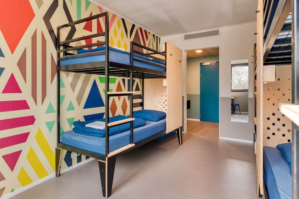 Une chambre avec des lits superposés, des murs ornés de motifs géométriques, une porte donnant sur une autre pièce et une fenêtre avec vue.