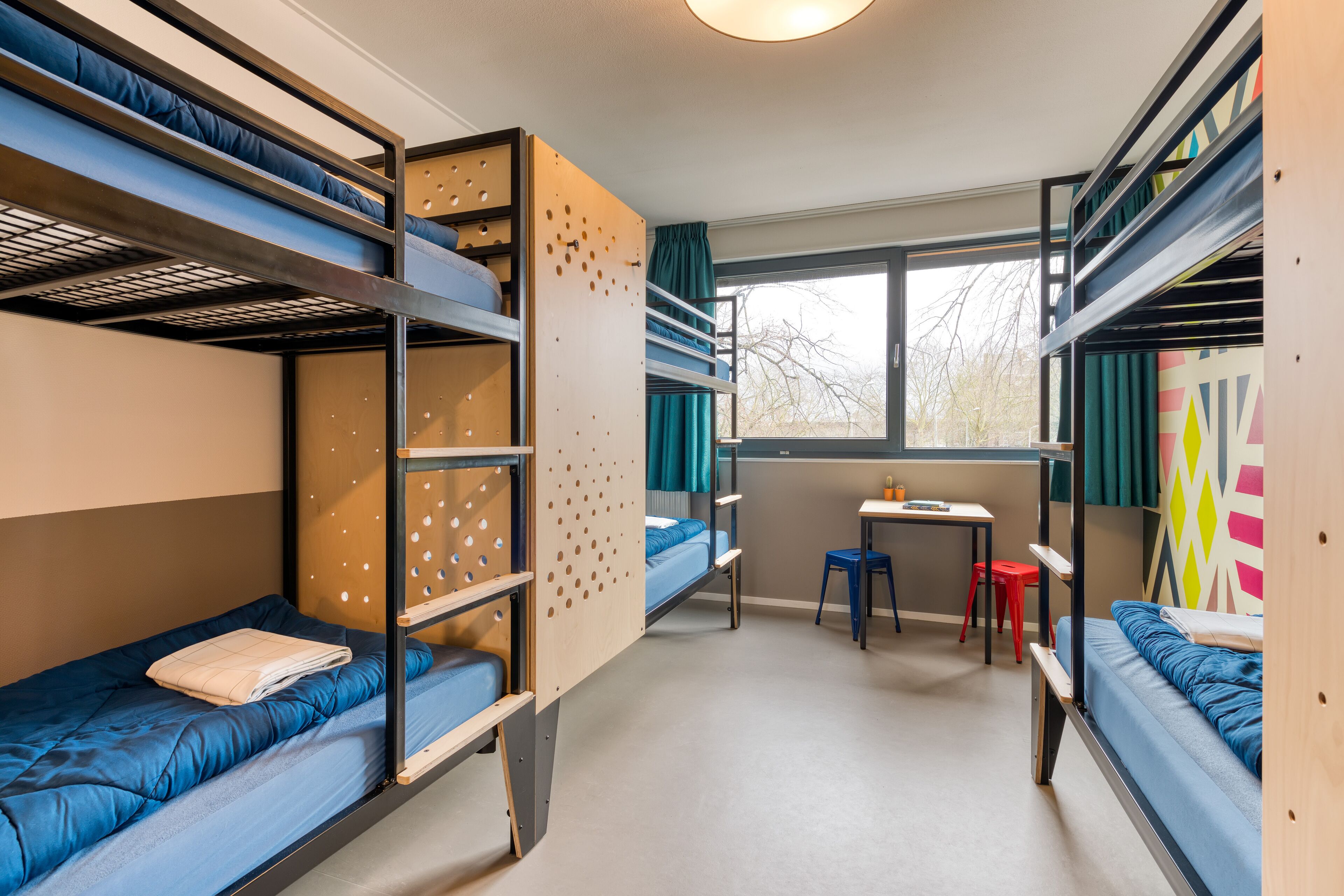 Une chambre de dortoir avec des lits superposés, un petit bureau et une fenêtre avec des rideaux.