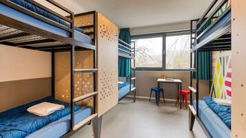 Une chambre de dortoir avec des lits superposés, un petit bureau et une fenêtre avec des rideaux.
