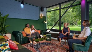 A modern living room with a green sofa, a coffee table, and a large window offering a view of the outdoors. - Stayokay Maastricht - Hostel (Maastricht)