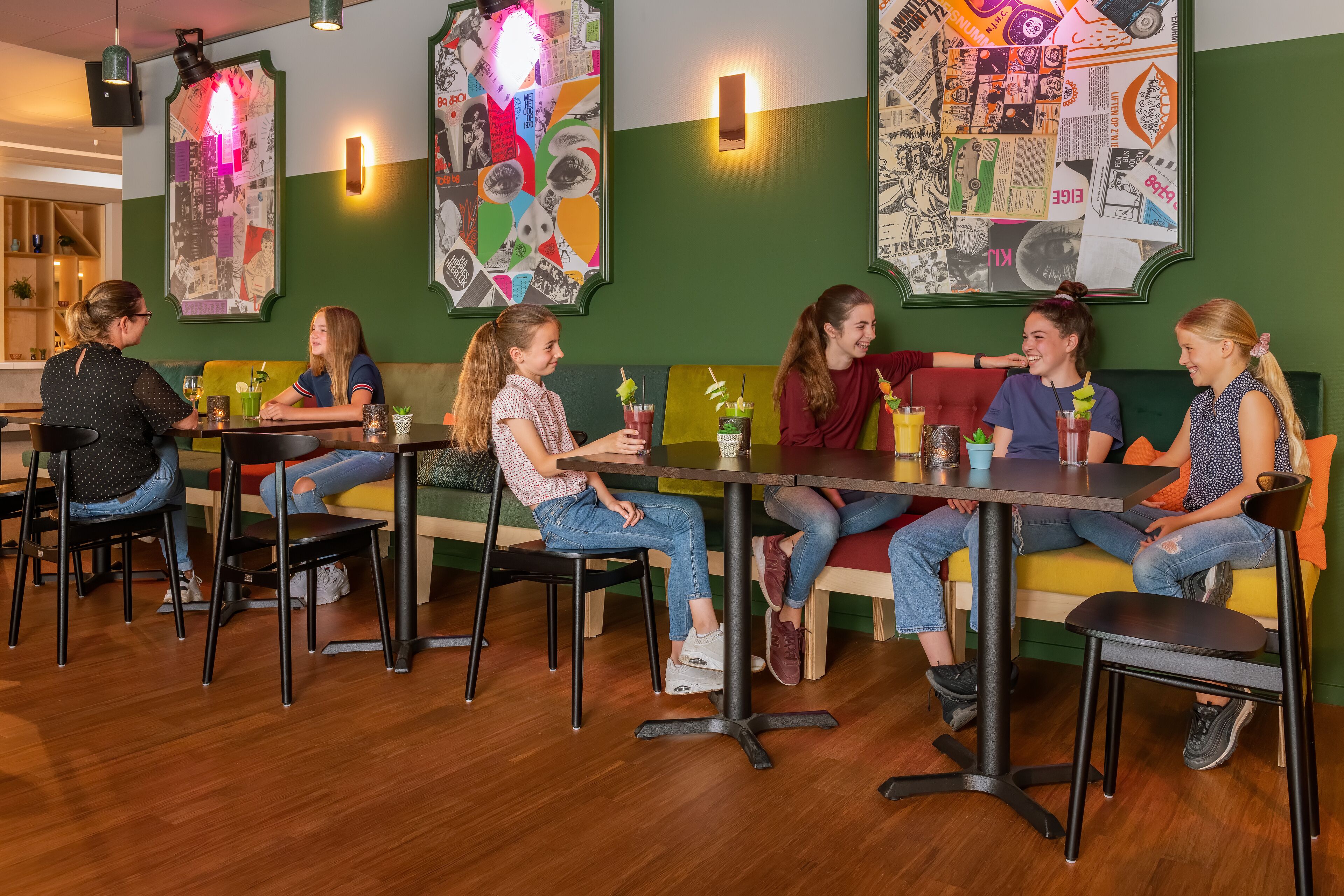 A group of people seated at tables in a cafe with green walls and artwork.