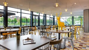 A spacious dining area with large windows, yellow chairs, and a prominent deer sculpture. - Stayokay Maastricht - Hostel (Maastricht)