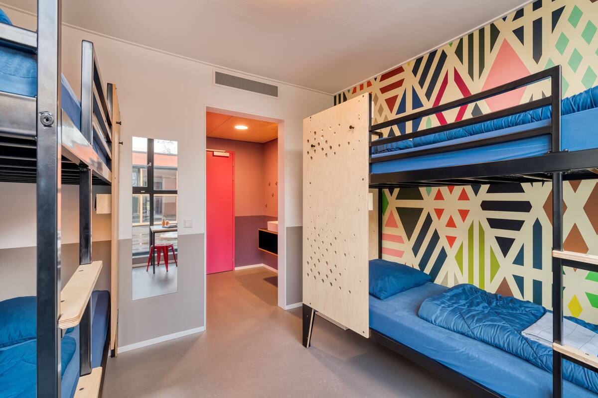 Une chambre de dortoir avec des lits superposés, une cloison en bois et un motif géométrique coloré sur le mur.